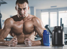 L'uomo muscoloso si siede sudorazione in palestra con tazza da bere e supplemento.