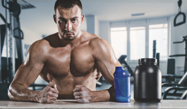 L'uomo muscoloso si siede sudorazione in palestra con tazza da bere e supplemento.